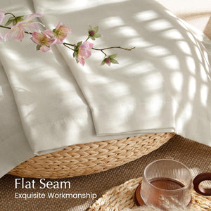 Off-white linen curtain showcasing flat seam and fine workmanship, folded in a woven basket with pink flowers.
