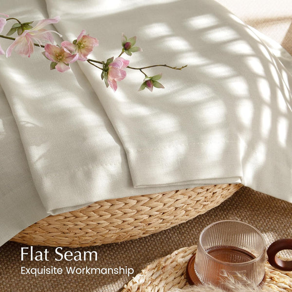 Off-white linen curtain showcasing flat seam and fine workmanship, folded in a woven basket with pink flowers.