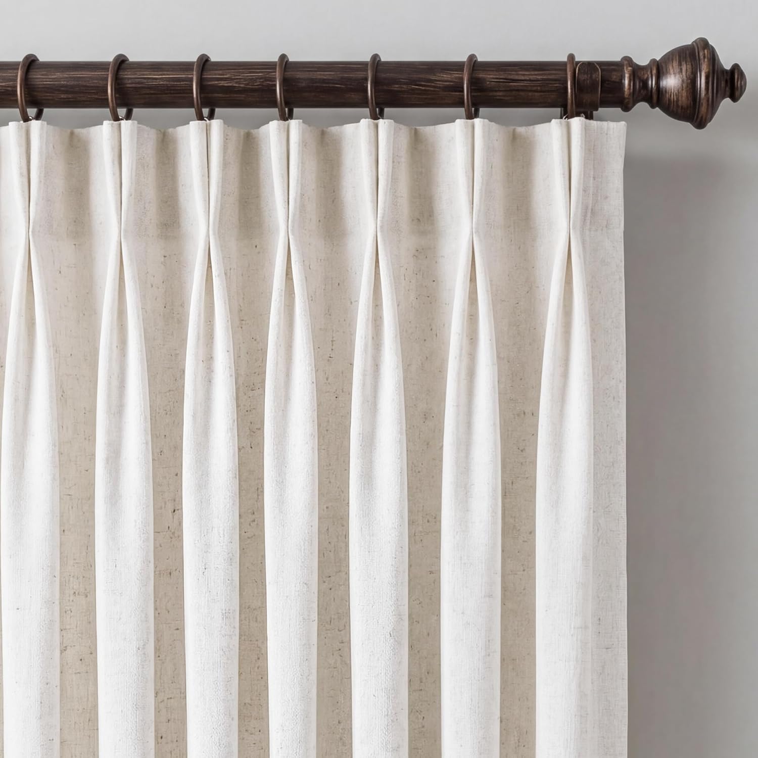 Off-white linen pinch pleat curtains hung on a dark bronze rod with decorative finial.