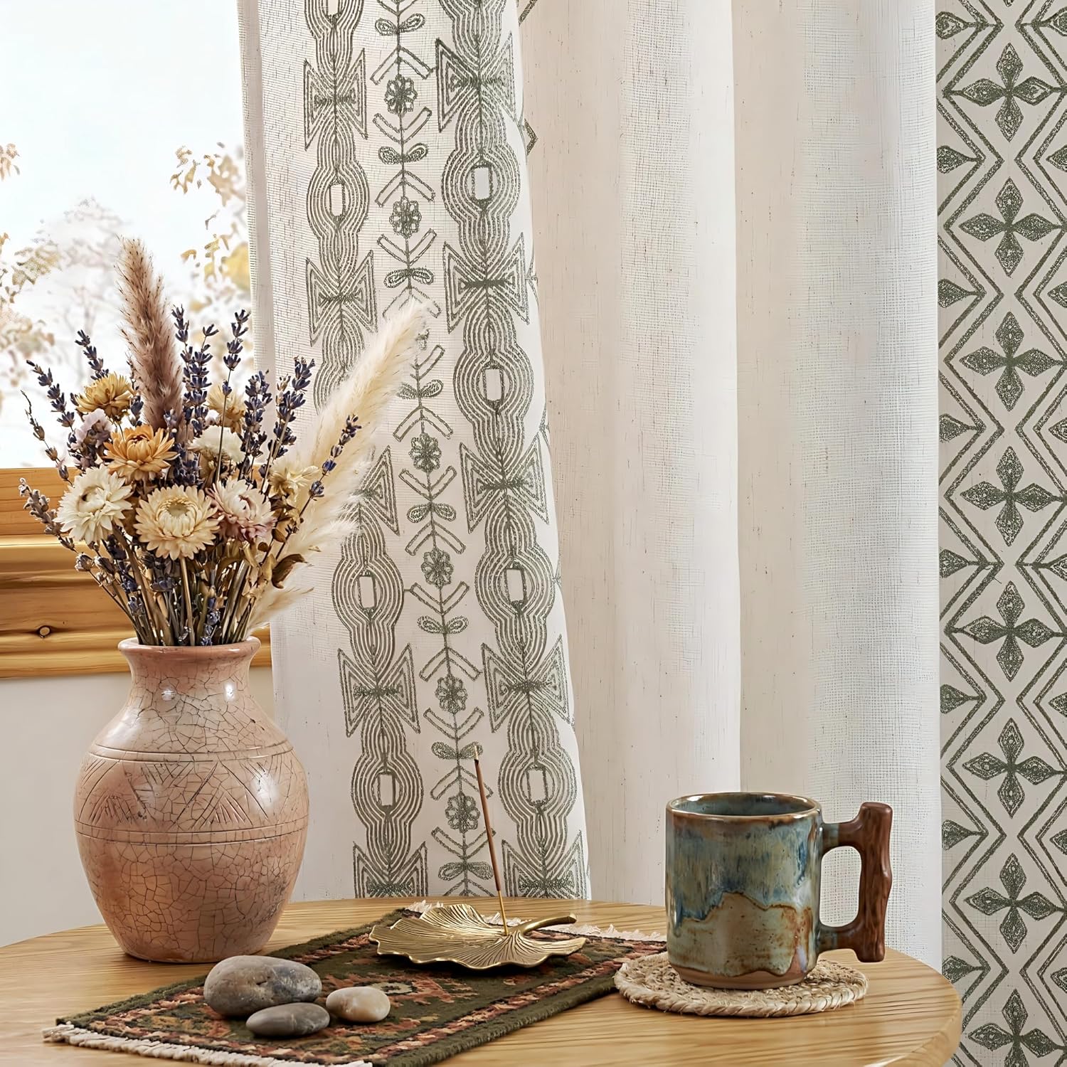 Off-white linen-blend curtains with sage green geometric tribal embroidery pattern, hanging in a bright window.