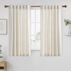 Off-white linen tab top curtains hanging on a wooden rod, filtering light in a bright room.