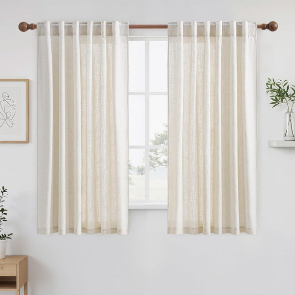 Off-white linen tab top curtains hanging on a wooden rod, filtering light in a bright room.