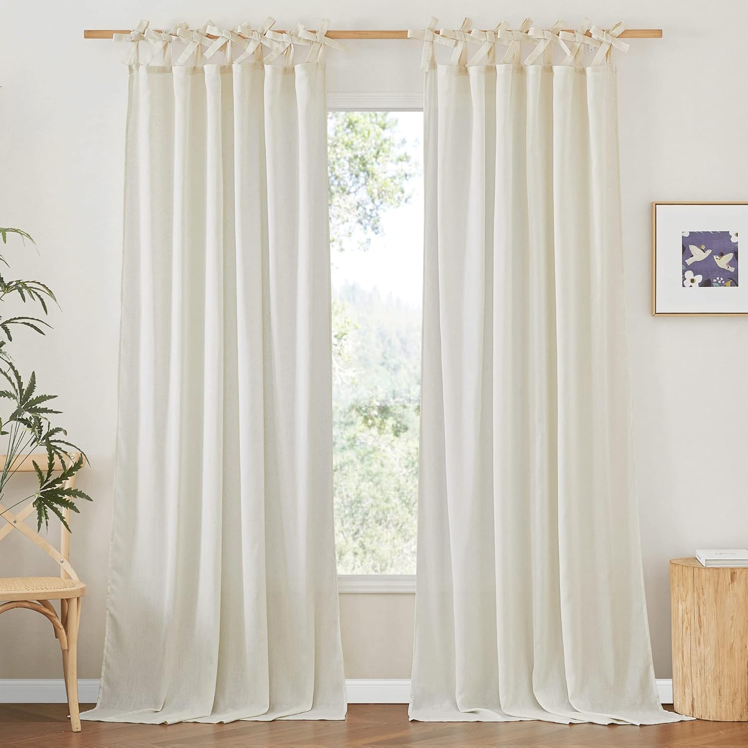 Pair of light off-white linen tie-top curtains hanging from a wooden rod, gracefully touching the floor.