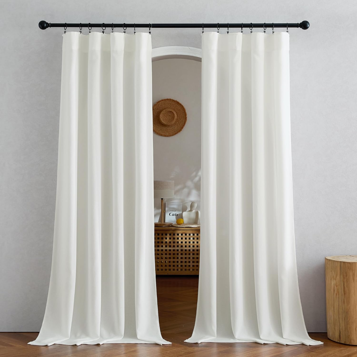 Full-length off-white pleated curtains hanging on a black rod, pooling gently on wooden floor.