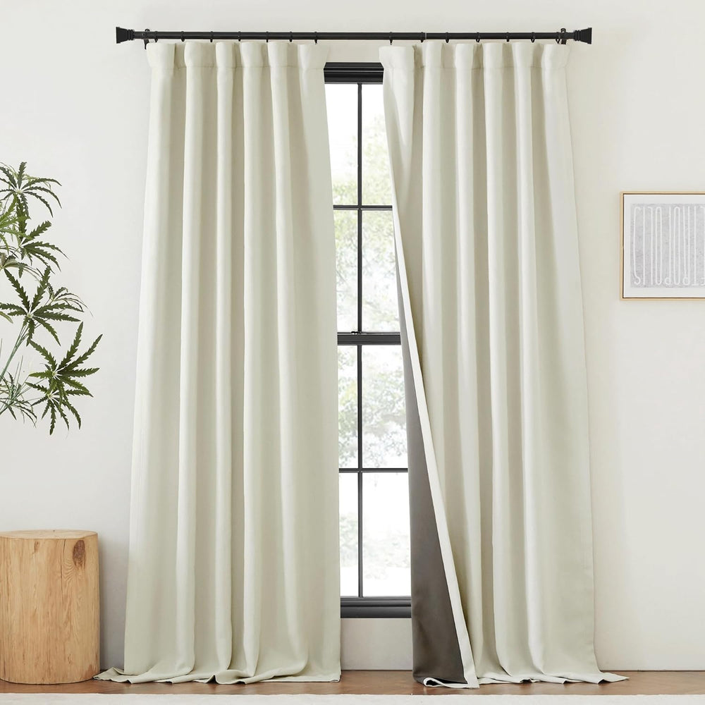 Off-white rod pocket blackout curtains with dark lining, hung on a black rod, one panel partially open.