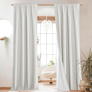 Off-white rod pocket blackout curtains with thick fabric hanging on a wooden rod in a bright room.