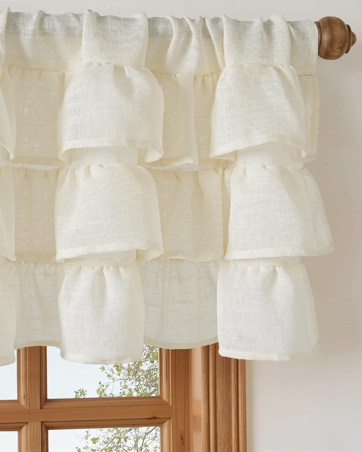 Off-white ruffled linen-look valance on a wooden rod above a window, showing tiered design.