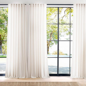 Floor-length off-white tab top drapes hung on black rods, framing tall windows with a view outside.
