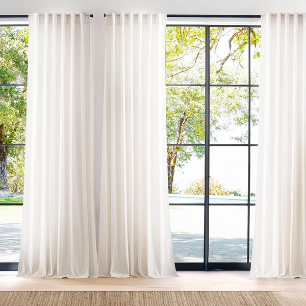 Floor-length off-white tab top drapes hung on black rods, framing tall windows with a view outside.