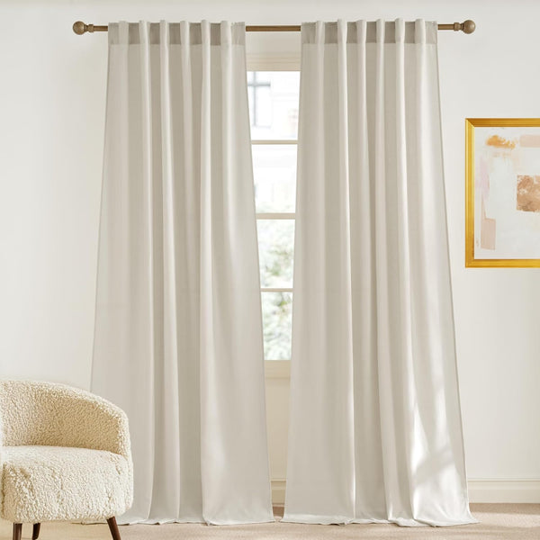 Pair of off-white tab top curtains softly filtering light from a window in a modern room.