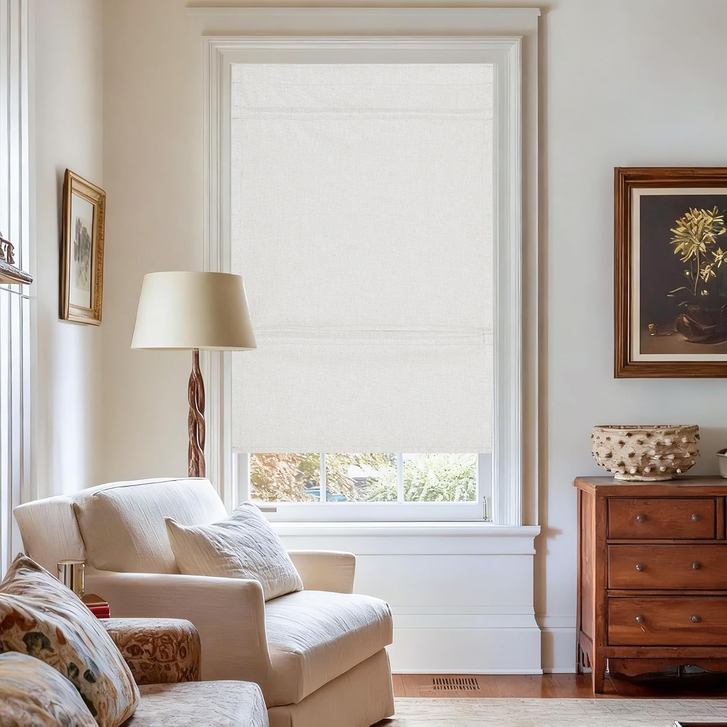 Light beige textured fabric flat Roman shade covering a window in a bright living room setting.
