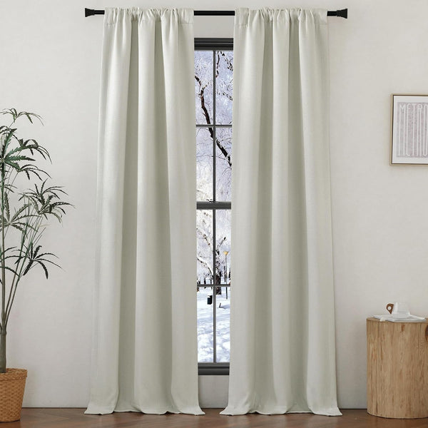 Off-white textured rod pocket curtains hanging on a black rod, framing a snowy window view.