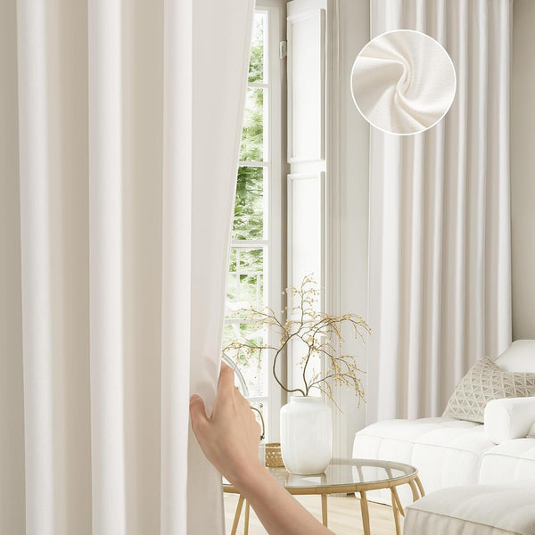 Off-white textured room darkening curtains hanging in a modern living room. A hand gently pulls the fabric, with an inset showing a close-up of the woven material.