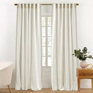 Pair of off-white curtains with subtle brown vertical ticking stripes hanging on a brass rod.