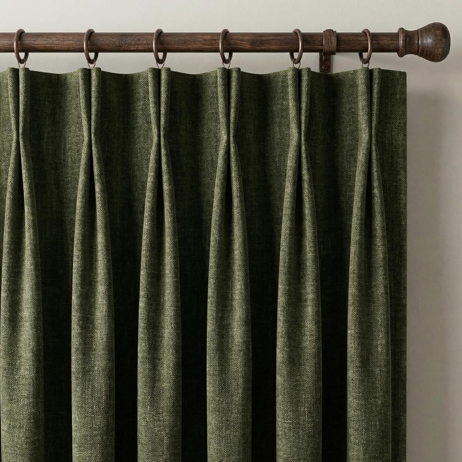 Close-up of olive green textured pinch pleat curtains hanging on a dark wood rod with rings.