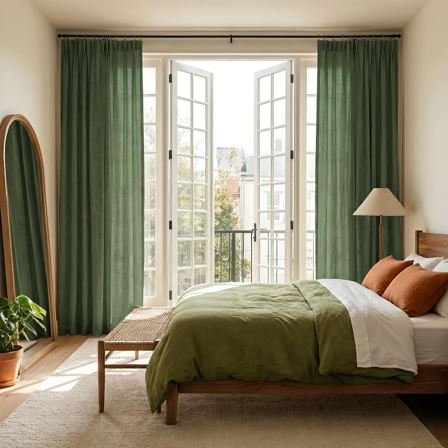 Pair of olive green linen curtains with pleated tops, hanging from a black rod over french doors in a bright bedroom.