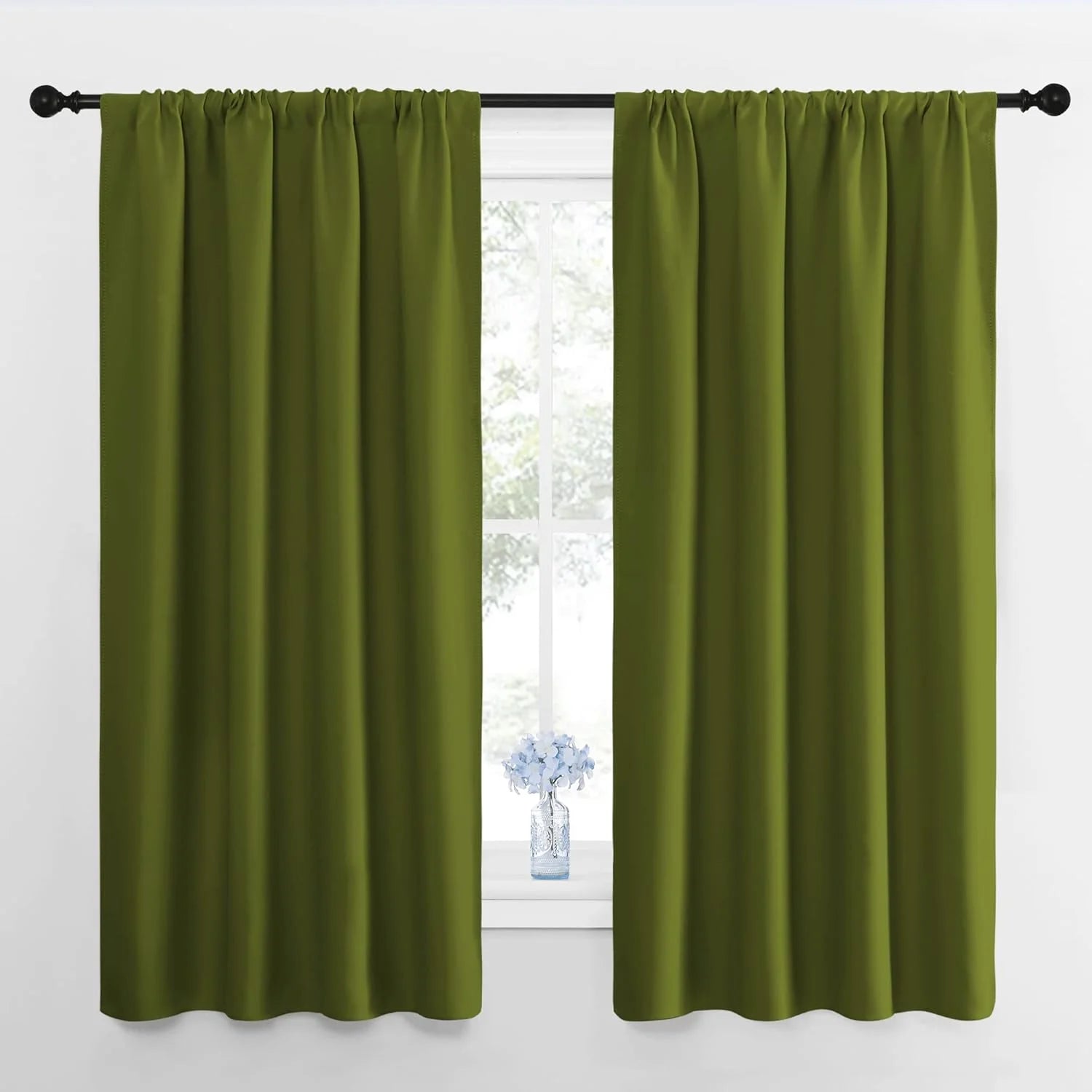 Pair of olive green blackout curtains with rod pocket top on a black rod, over a window with a vase.