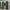Two dark green outdoor privacy curtains with silver grommet tops hanging from a white pergola on a patio.