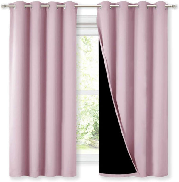 Pair of solid pink grommet top blackout curtains hanging on a silver rod, with one panel revealing its black lining against a window.