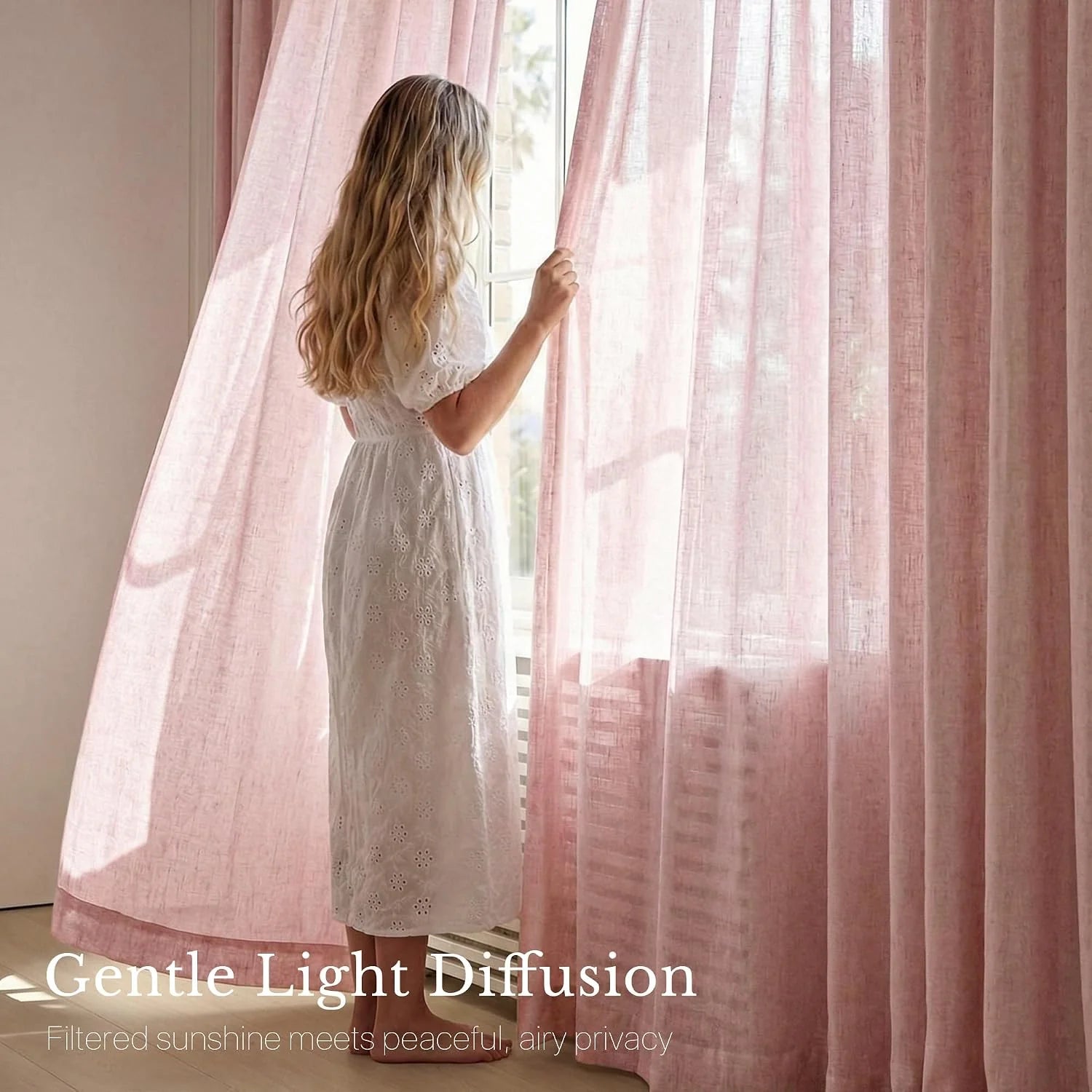 Woman in white dress by window, gently holding sheer pink light-diffusing curtains.
