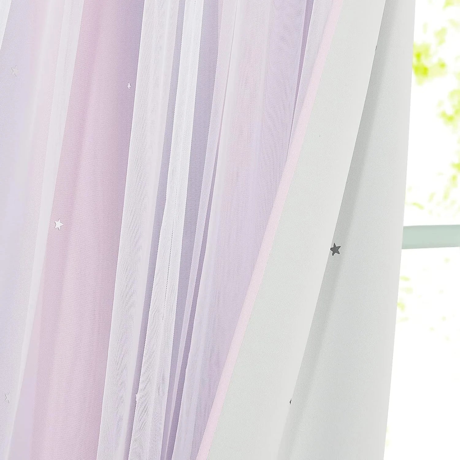 Soft pink sheer curtain with small star details hanging by a bright window