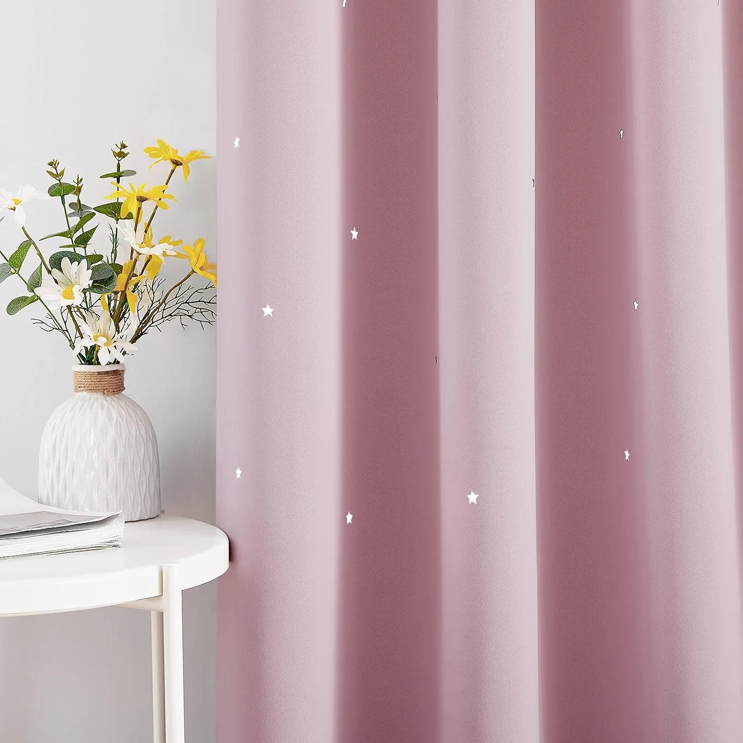 Pink curtain panel with small white stars beside a white table and flower vase
