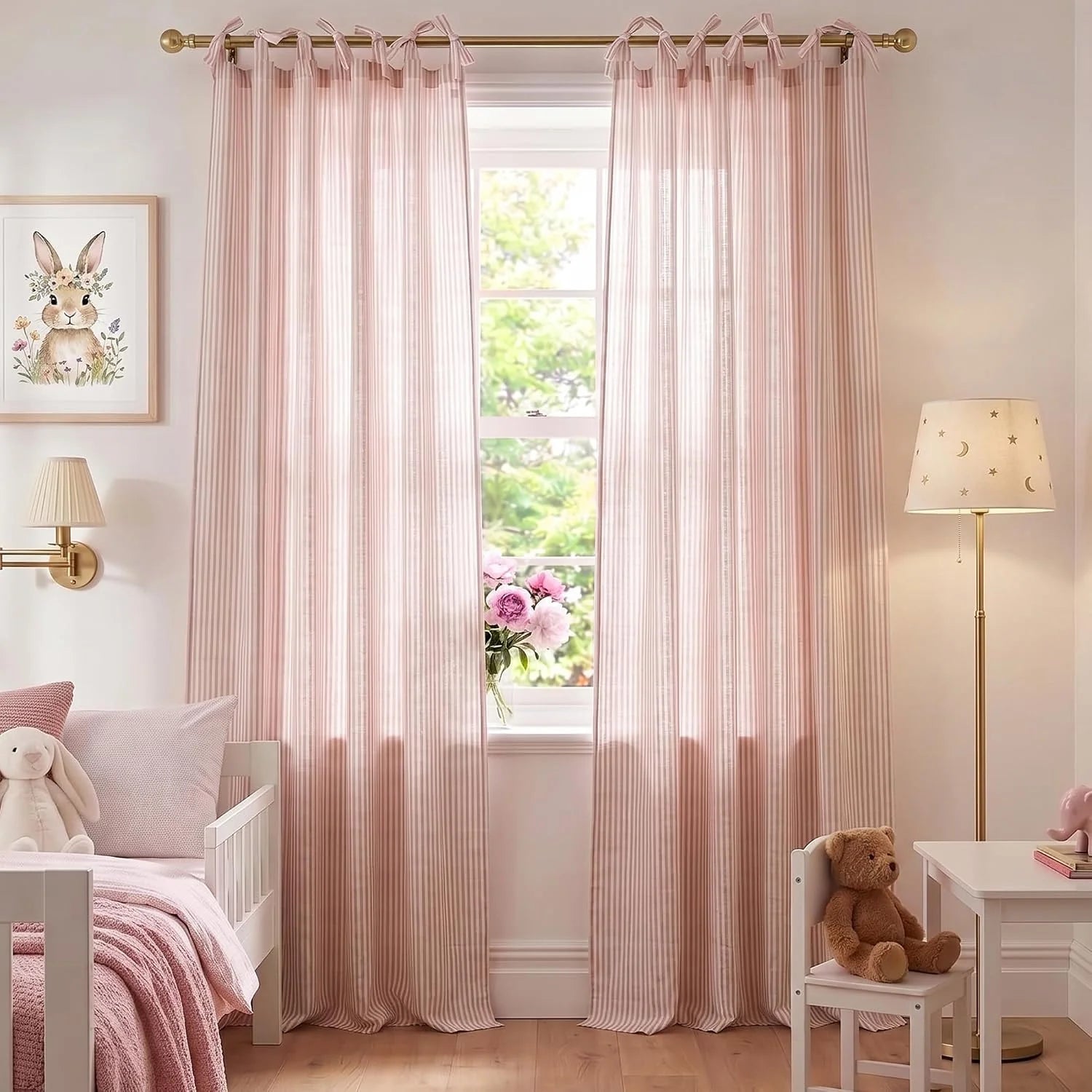 Light pink striped tie-top curtains on a gold rod in a charming nursery with a white bed and bunny art.