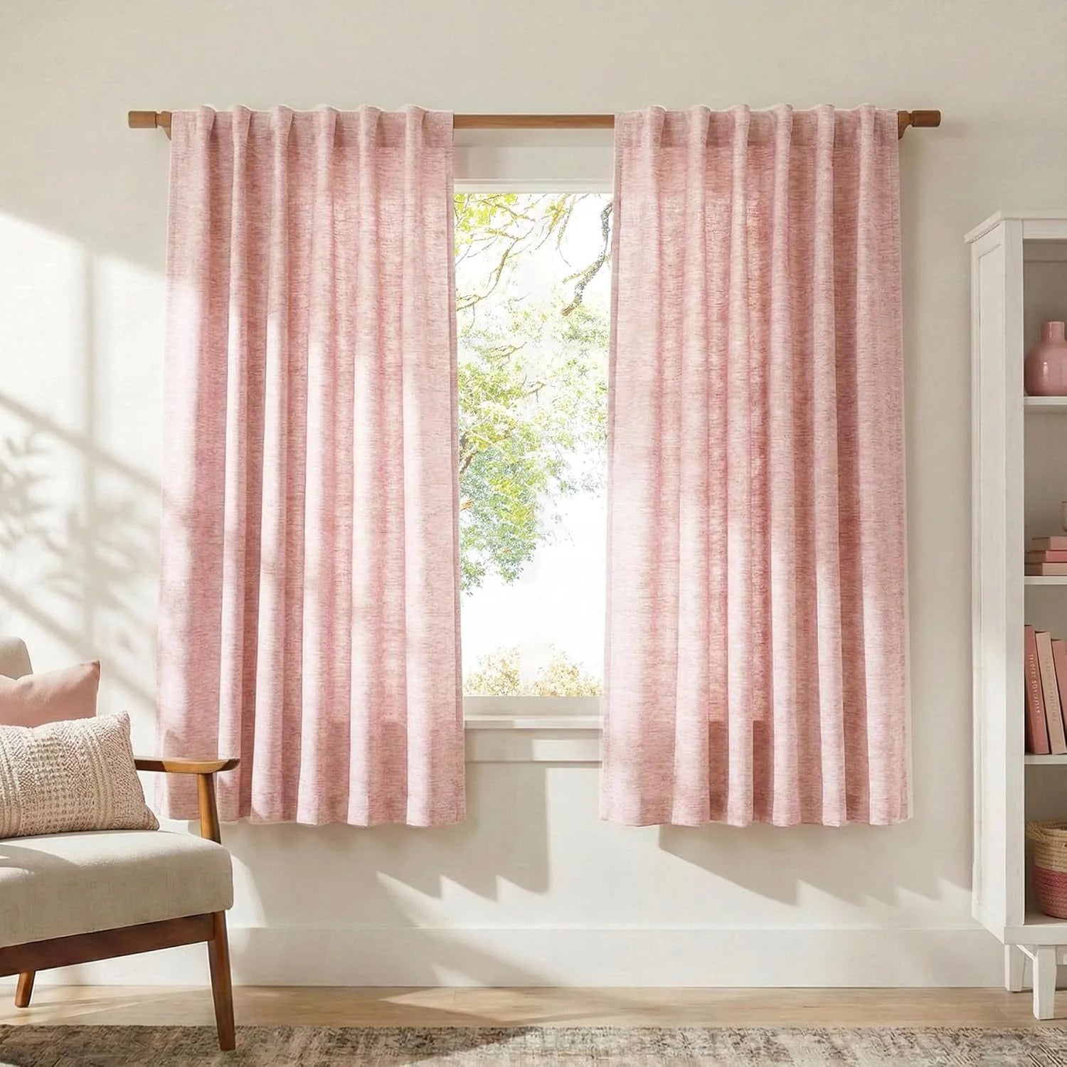 Pink textured curtains with a rod pocket hanging on a wooden rod in a sunlit room.
