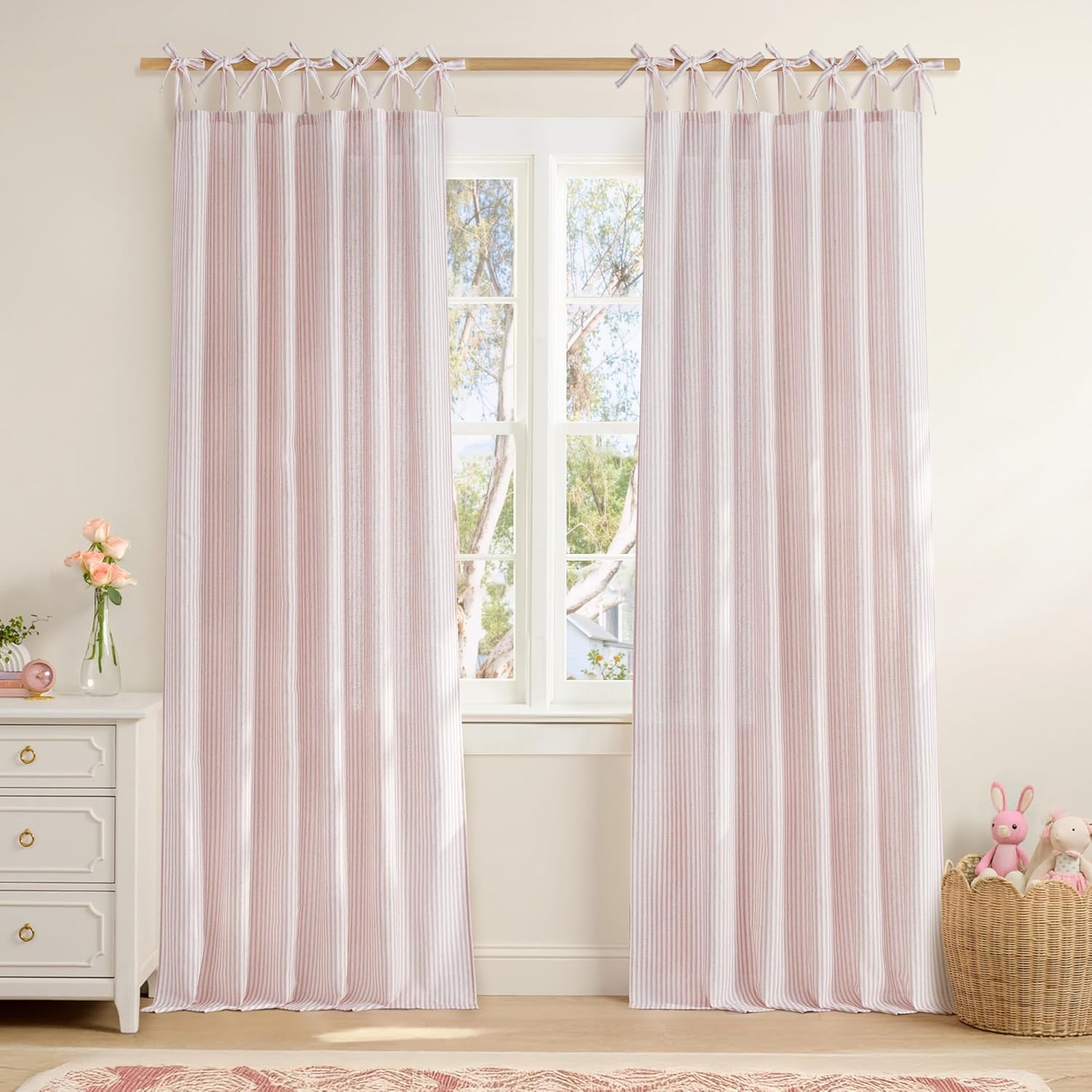 Pink and white ticking stripe tie top curtains hanging on a wooden rod in a bright room.