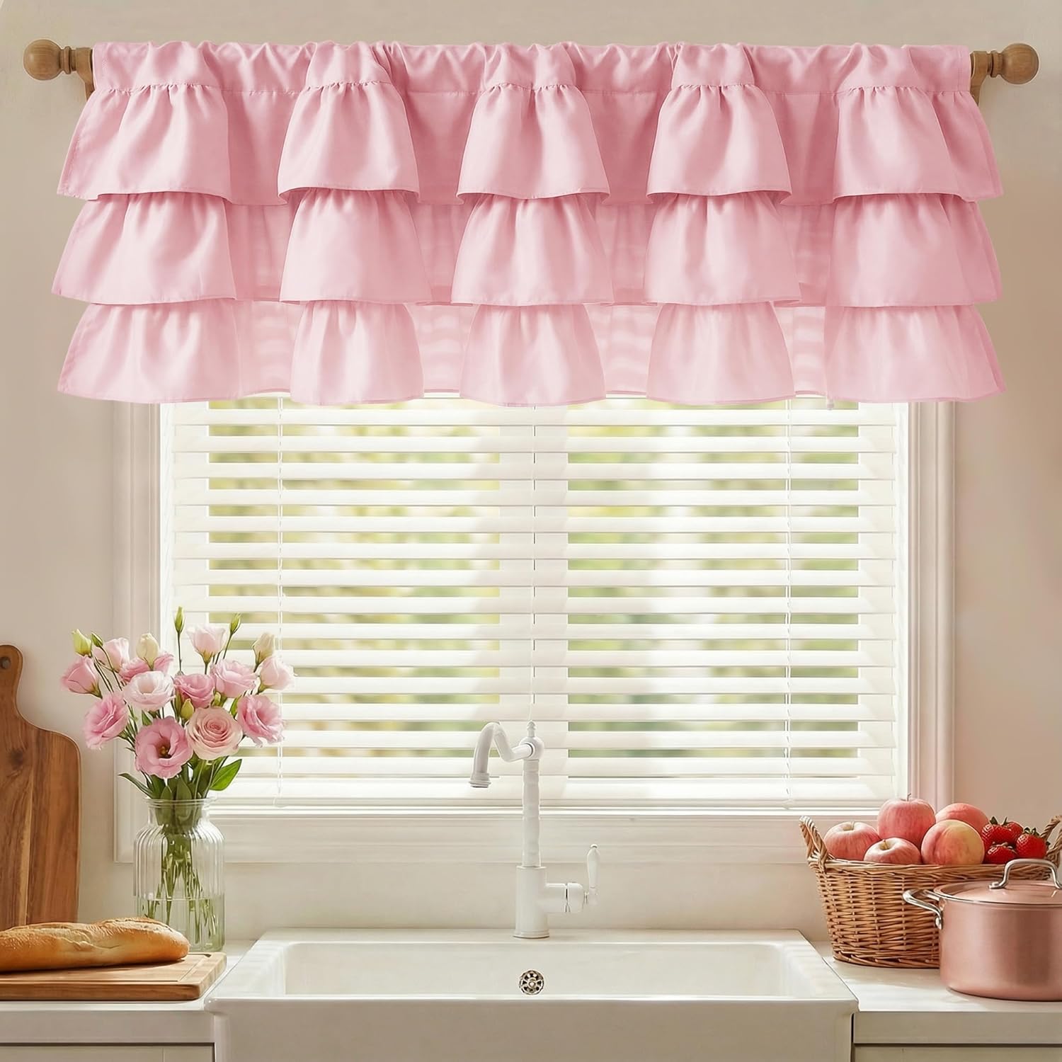 Light pink three-tiered ruffle valance hanging above a kitchen window with white blinds.