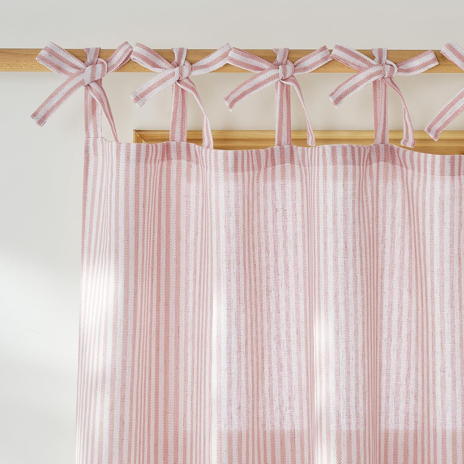 Pink and white striped tie-top curtain with decorative bows on a wooden rod, showcasing textured fabric.