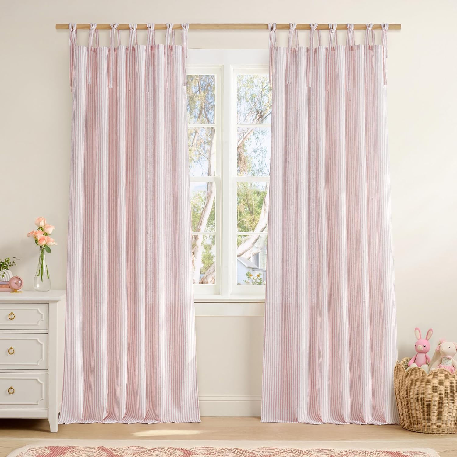 Light pink and white ticking stripe tie-top curtains hanging in a bright bedroom setting.