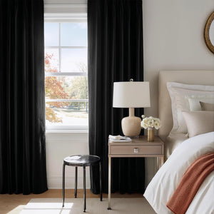 Plush black velvet curtains with rich folds are drawn across a window in a stylish bedroom setting.
