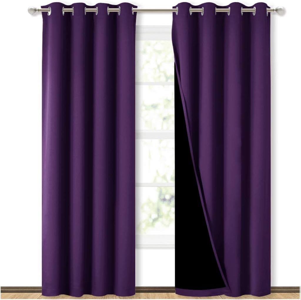 Two rich purple grommet top blackout curtain panels hanging on a silver rod, showing black lining.