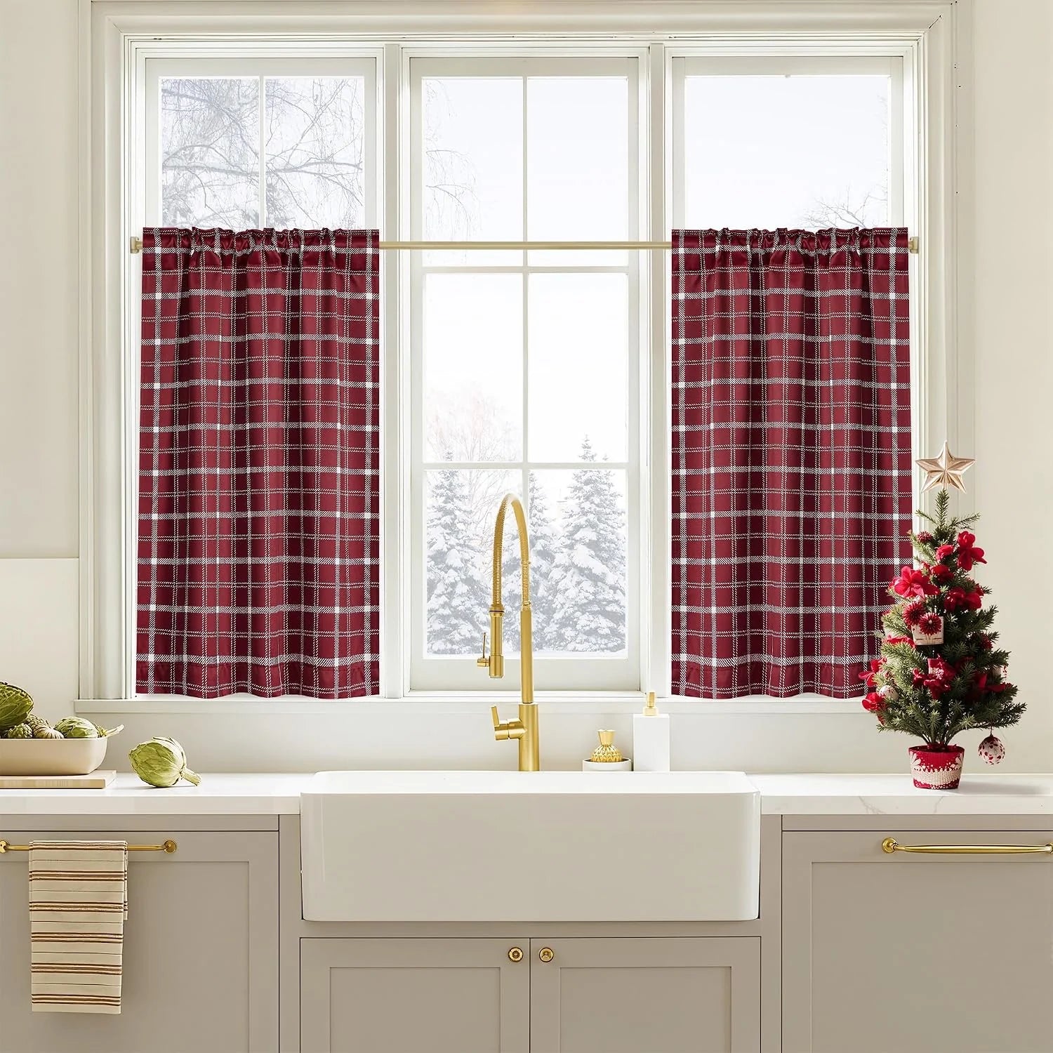 Red plaid tier curtains over a bright kitchen sink with brass faucet and holiday decor