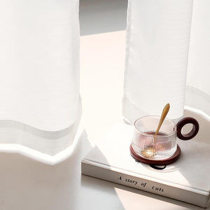 Clear ribbed glass mug with dark wood handle and coaster, gold spoon, on book by window.