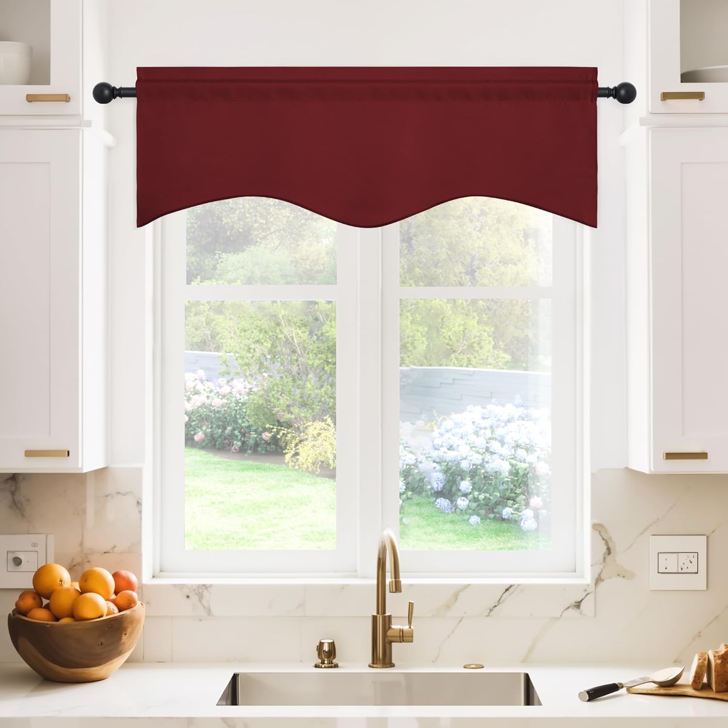 Rich burgundy fabric valance with a wavy, scalloped bottom edge hanging on a black rod above a kitchen sink window.
