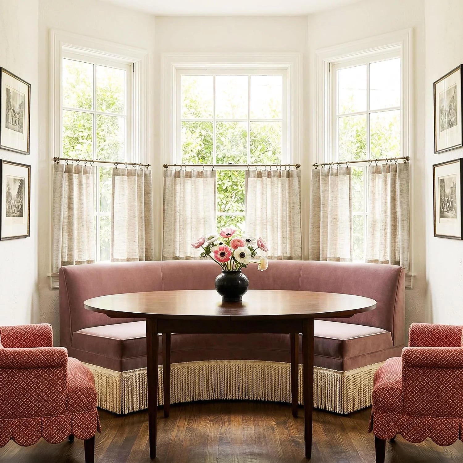Elegant dining nook with a dusty rose fringed banquette, round wood table, and patterned chairs.