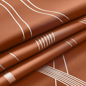 Close-up of rust brown fabric with shimmering silver geometric lines, folded to show texture and pattern.