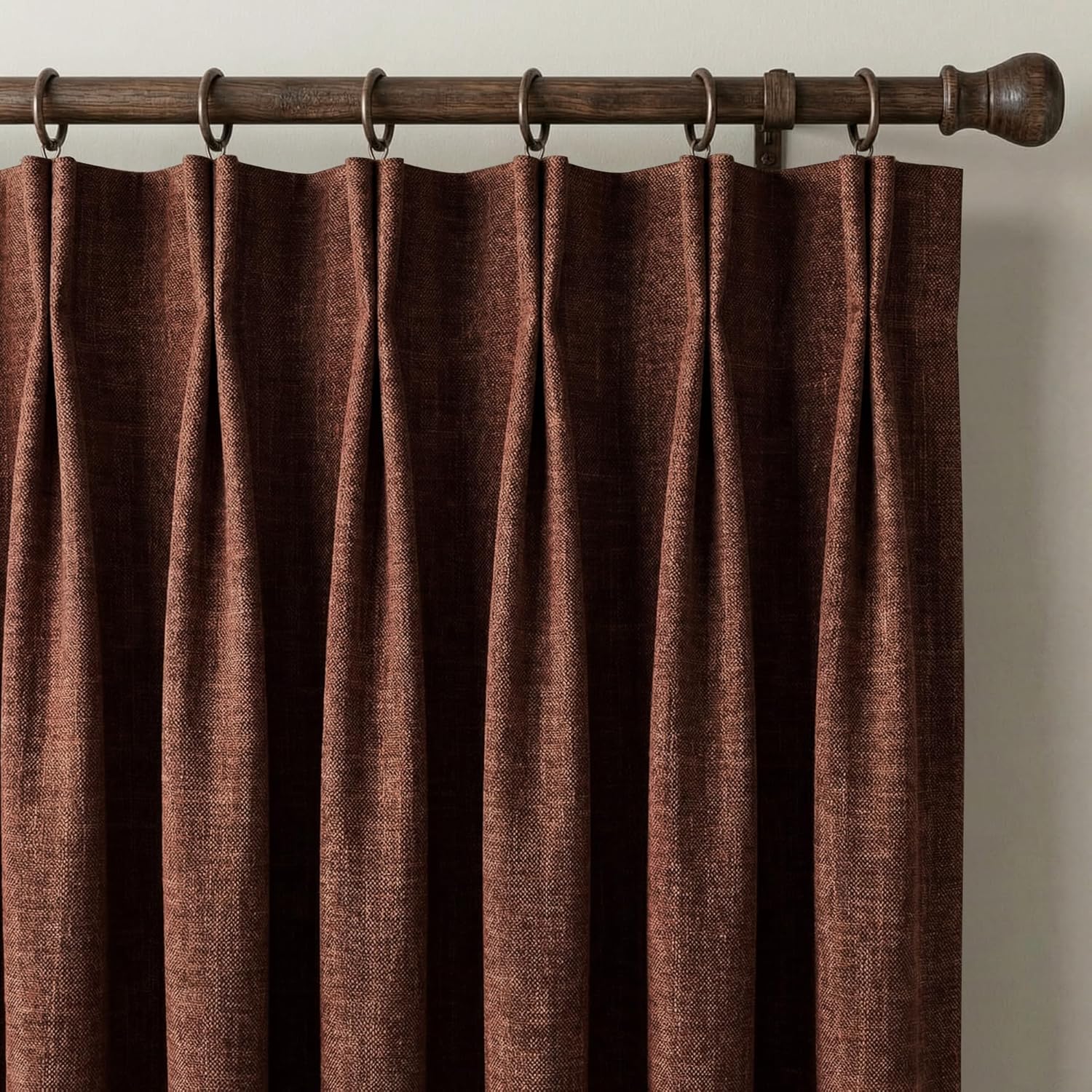 Close-up of rust brown textured pleated curtains, hung from a dark wooden rod with bronze rings.