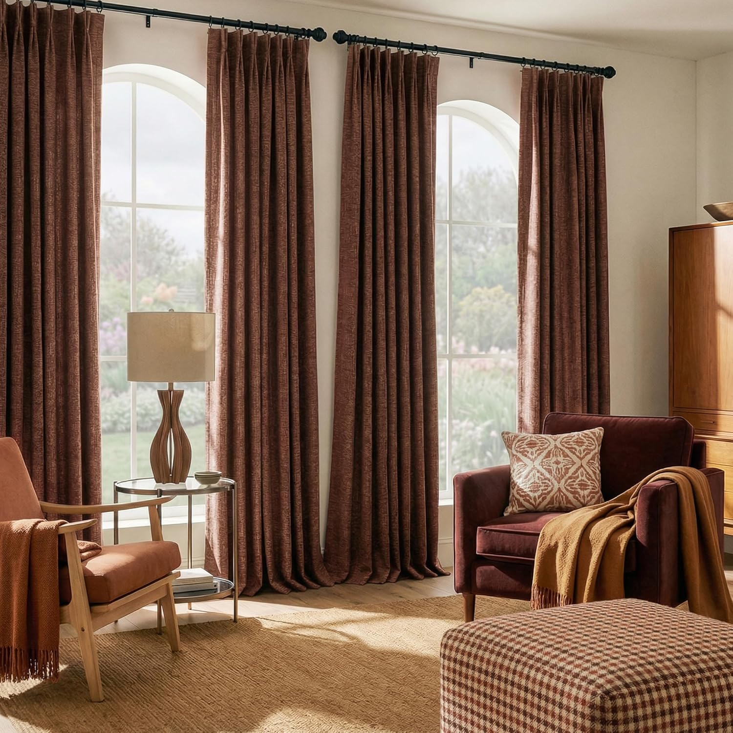 Deep rust brown textured pleated curtains on black rods framing arched windows in a warm, inviting living room.