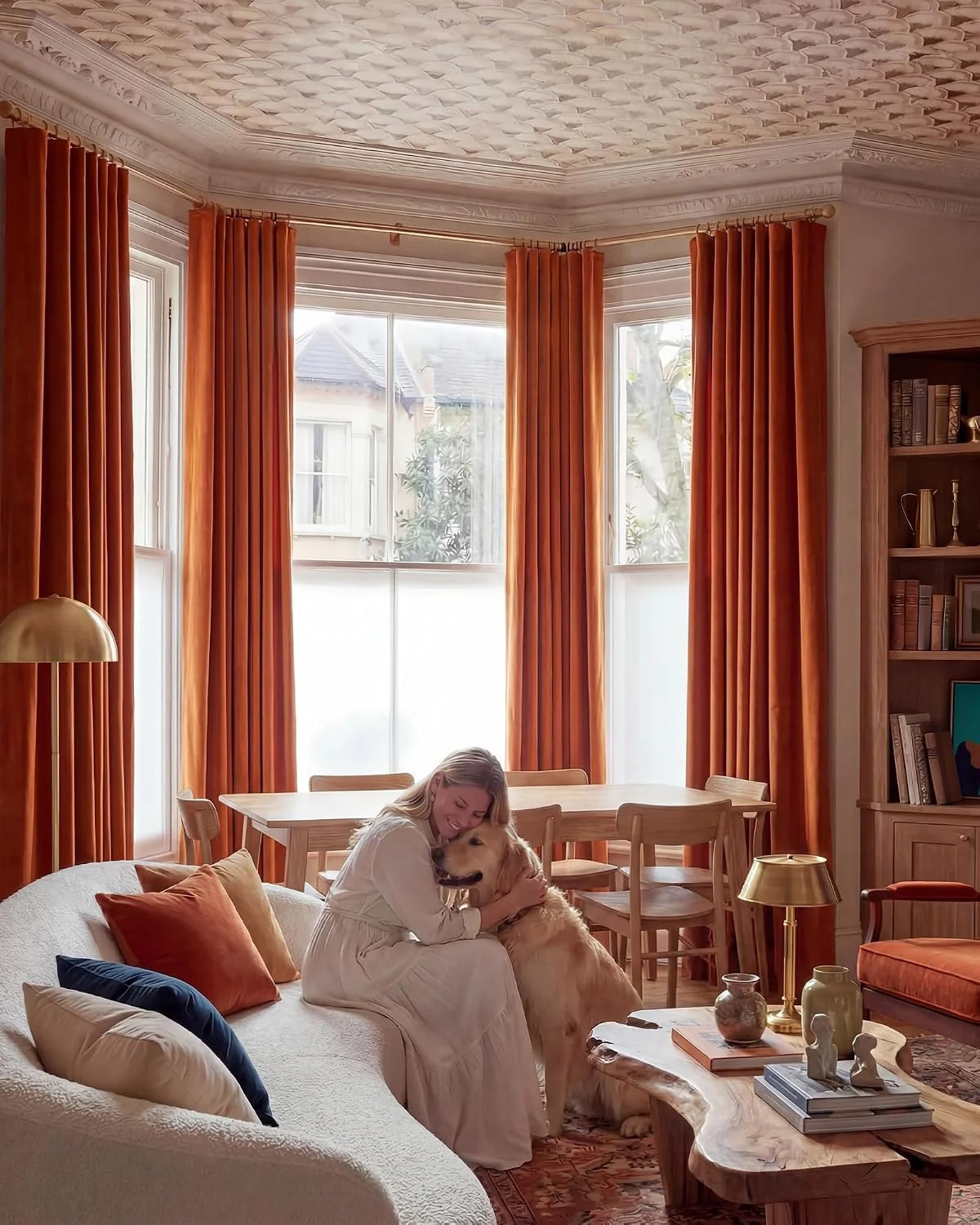 Rust orange velvet curtains in a warm living room with a woman hugging a golden retriever