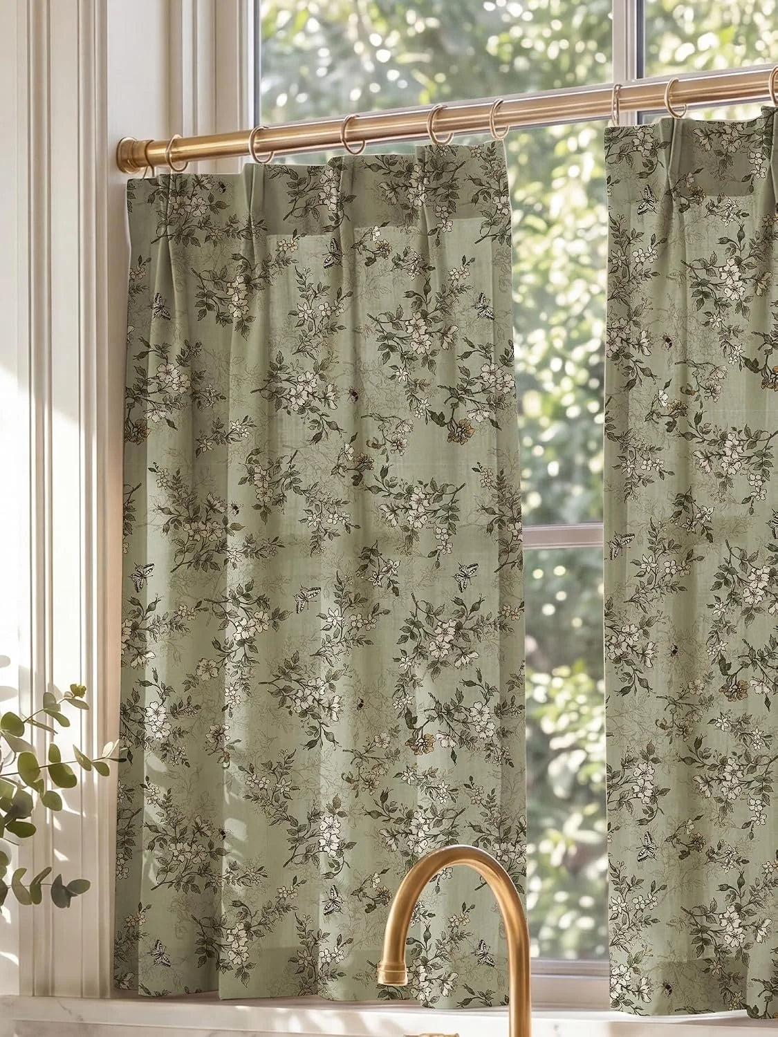 Sage green floral cafe curtains on brass rings hanging in a sunlit kitchen window