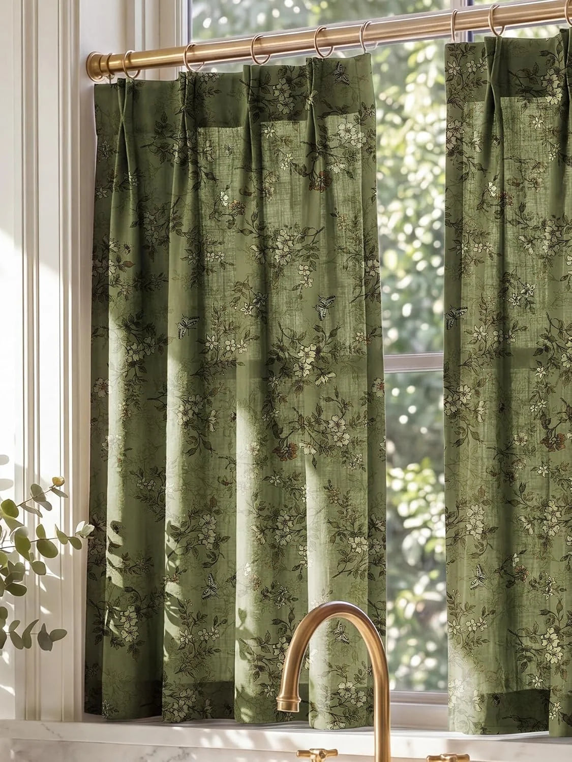 Sage green floral cafe curtains with ring top on a brass rod in a sunlit kitchen window