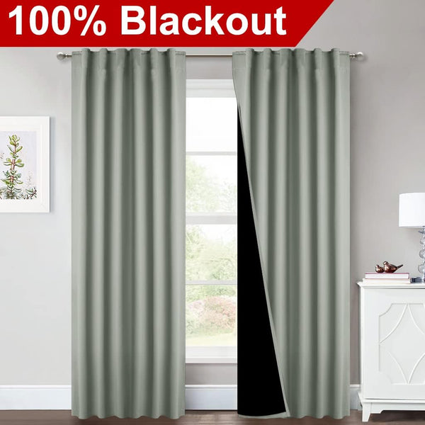 Muted sage green blackout curtains with back tabs hanging over a window, revealing a black thermal lining.