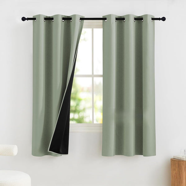 Sage green blackout curtains with grommet top, one panel open showing thick black lining, hanging on black rod.