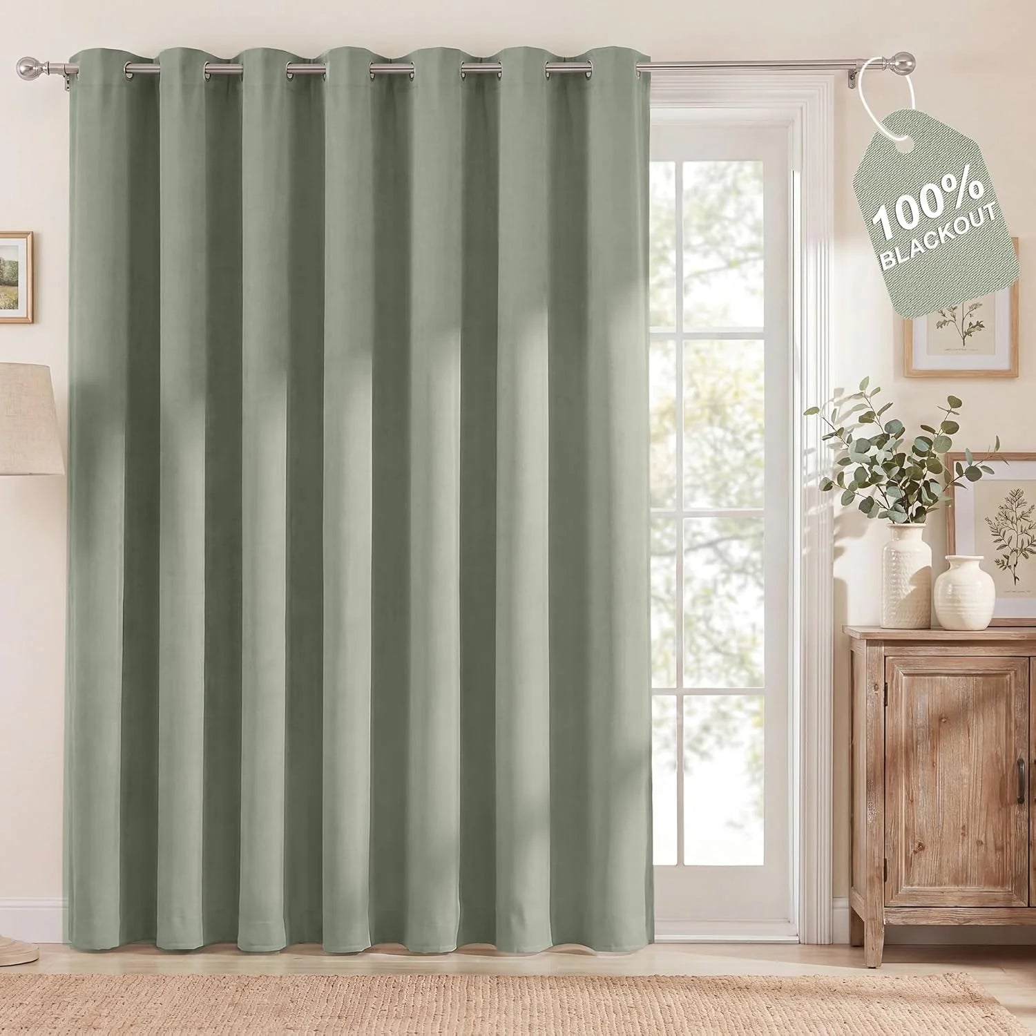 Muted green full-length blackout curtain with silver grommets in a cozy living space, showing a '100% Blackout' tag.
