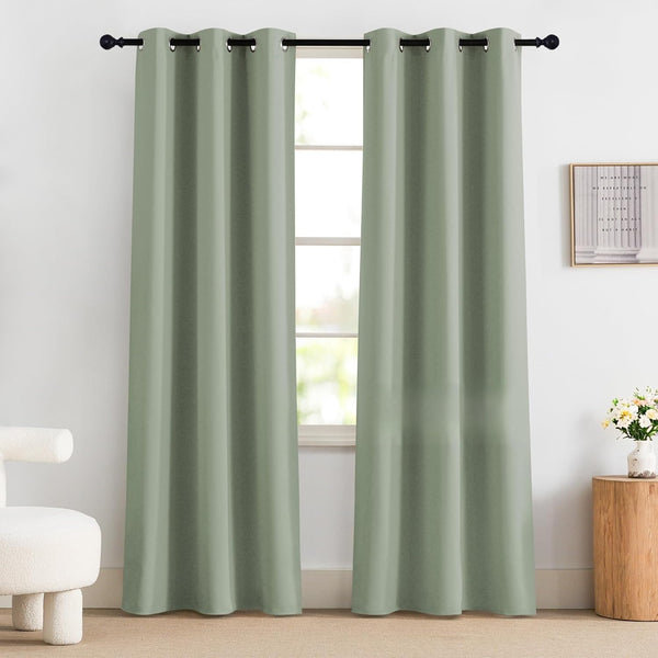 Two solid sage green grommet top curtain panels on a black rod, framing a window in a bright room.
