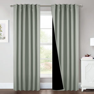 Pair of sage green grommet top blackout curtains hanging on a silver rod, with one panel showing its dark lining.