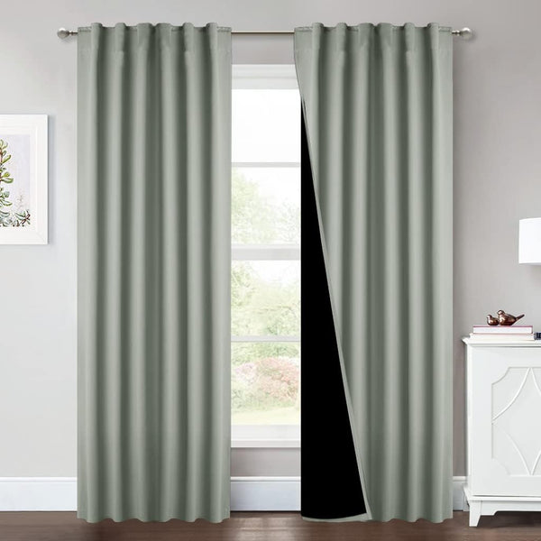 Pair of sage green grommet top blackout curtains hanging on a silver rod, with one panel showing its dark lining.